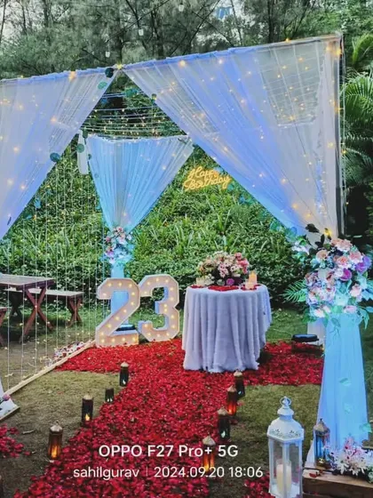 An outdoor garden setup for a 23rd birthday or anniversary. I laid out a red rose petal carpet, framed by lanterns and a canopy of fairy lights, creating a magical celebration space.
