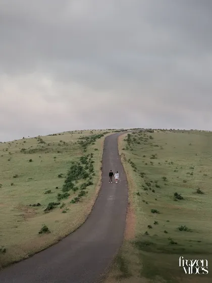 A dramatic wide shot of Monil and Charmi walking along a lonely road that winds through rolling green hills. This kind of image tells a story of a journey shared together.