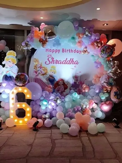 A dreamy Disney Princess birthday party for a 6-year-old. The decor features a custom backdrop with multiple princesses, a marquee number '6', and pastel-colored balloons.