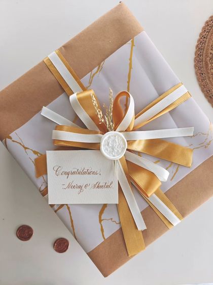 A beautifully wrapped anniversary gift, featuring gold and white ribbons, a wax seal, and a handwritten congratulations card for the couple.