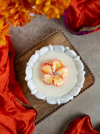 This marble urli candle features a stunning, hand-colored wax flower in the center. The vibrant orange and yellow hues are perfect for the festive season.