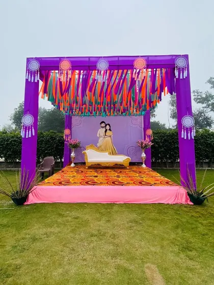 A simple and colorful outdoor setup for a Haldi or Mehendi ceremony. The purple draping is accented with vibrant ribbon tassels and dreamcatchers for a bohemian touch.