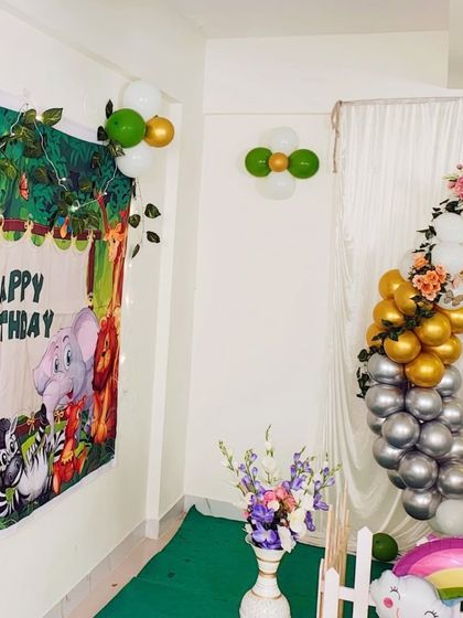 A partial view of a jungle-themed birthday setup, showing a printed animal backdrop next to the main circular balloon arch decoration.
