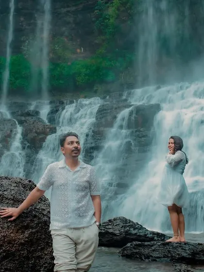 An artistic, moody shot of the couple at the waterfall. They stand apart, looking in different directions, creating a cinematic and thought-provoking image.