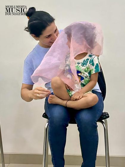 A mother and child share a playful moment with a scarf in our parent-toddler class. Using props like scarves helps children visualize musical phrases and develop motor skills.
