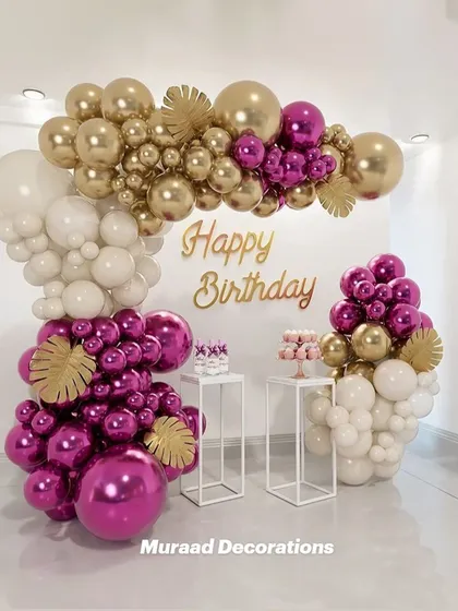 This modern and chic birthday setup uses a striking color combination of magenta, gold, and white. The asymmetrical balloon arrangement and clean white pedestals create a very stylish and high-end look.