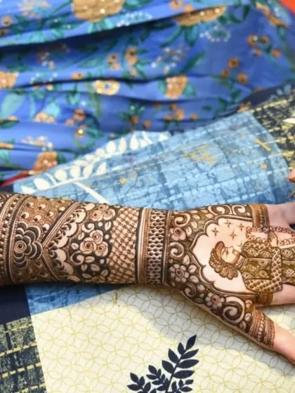 A side view of the bridal mehndi application in progress. You can see the intricate patterns taking shape on the arm, leading down to the beautiful portrait on the palm.