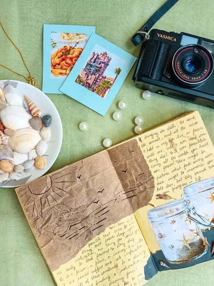 A beach-themed journal page featuring embossed paper and seashell decorations, styled with a vintage camera.