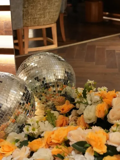 Disco balls nestled in a bed of orange and white flowers add a fun, retro-glam touch to a honeybee-themed baby shower.