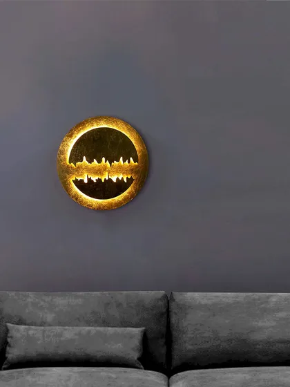 A similar sculptural wall light with a cityscape-like design. The golden finish and warm backlight create a festive and luxurious glow on the wall.