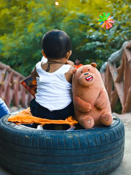 A candid shot from behind during the "little mechanic" session, showing the baby interacting with his teddy bear companion. This perspective adds a story-telling element to the themed baby photoshoot.