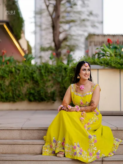 The bride sitting on the steps, looking radiant in her Mehndi outfit. A moment of calm and happiness before the wedding festivities.