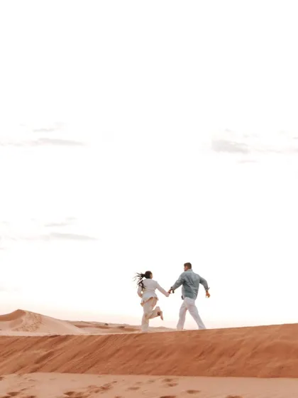 A sense of adventure and freedom as the couple runs hand-in-hand over the crest of a sand dune. This dynamic shot captures the joy of their shared journey.