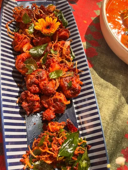 Our Nasrani-style prawn fry, beautifully plated on a striped dish. The prawns are garnished with fried onions and curry leaves, adding layers of texture and flavour.