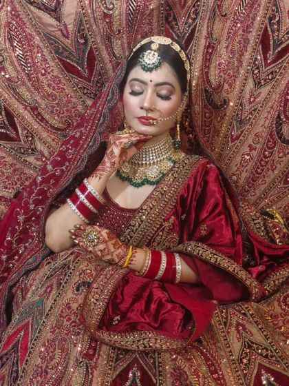 A bride enveloped in a luxurious red velvet lehenga with intricate gold embroidery. This is a classic, opulent look for a traditional wedding.