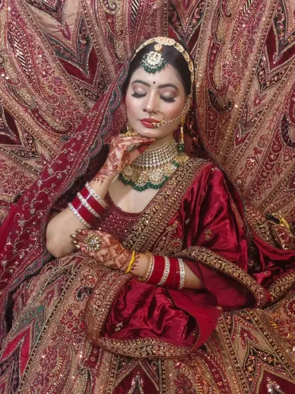 A bride enveloped in a luxurious red velvet lehenga with intricate gold embroidery. This is a classic, opulent look for a traditional wedding.
