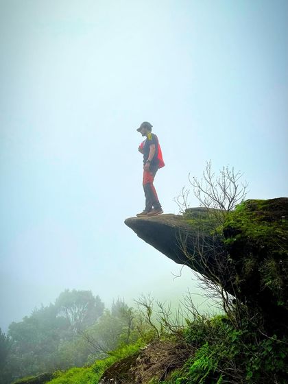 Standing on a dramatic rock ledge in the foggy landscape of the Western Ghats. These treks offer incredible photo opportunities and a real sense of adventure.