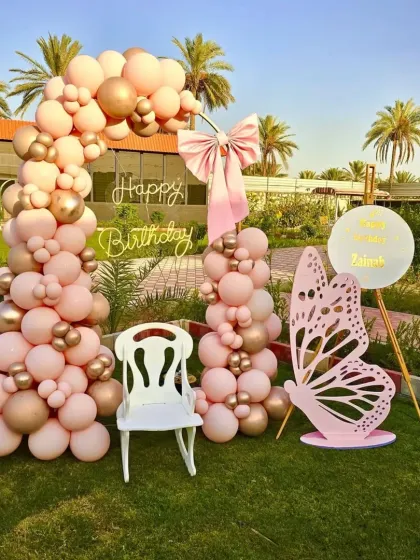 A wide shot of the elegant butterfly-themed outdoor setup, showing the full balloon arch and props against the beautiful green lawn.