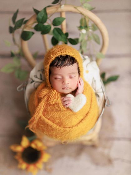 A little sunflower. The warm mustard wrap and sunflower props create a bright and cheerful scene for this sleeping baby.