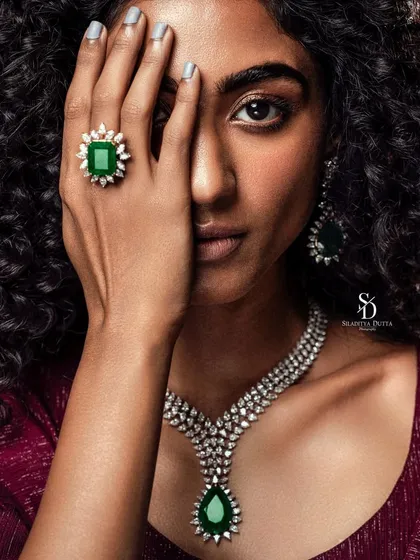 A dramatic jewellery shot where the model's face is partially obscured. This composition puts the focus squarely on the stunning emerald ring and diamond necklace.