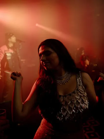 Khushboo enjoys the music at her engagement party, with the artist performing in the background. The red lighting and her relaxed vibe capture the atmosphere of a great party.