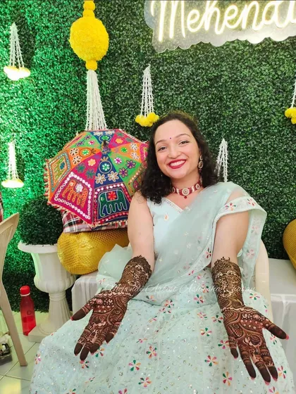 A beautiful bride posing with her full bridal mehendi. The intricate designs on her hands and arms complement her festive attire perfectly.