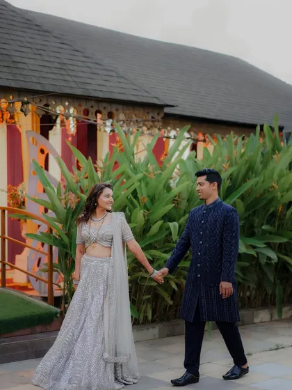 A full view of the couple's coordinated reception outfits. The bride's silver lehenga and the groom's navy sherwani create a stylish and modern look.