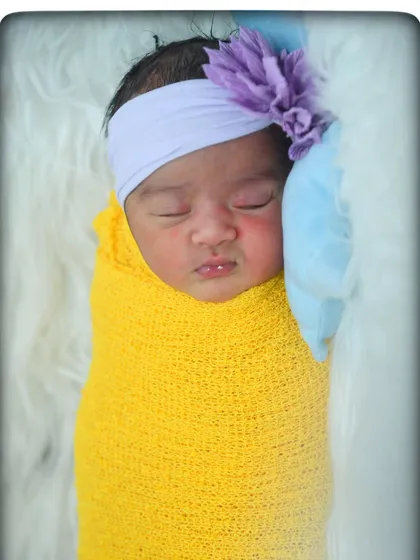 A close-up of a sleeping newborn, swaddled in yellow with a delicate purple floral headband. The details matter, from their tiny lips to their peaceful expression.