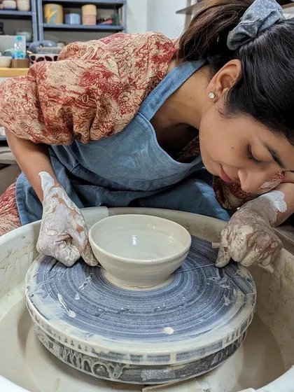 A student carefully uses a wire tool to cut her finished bowl off the potter's wheel.