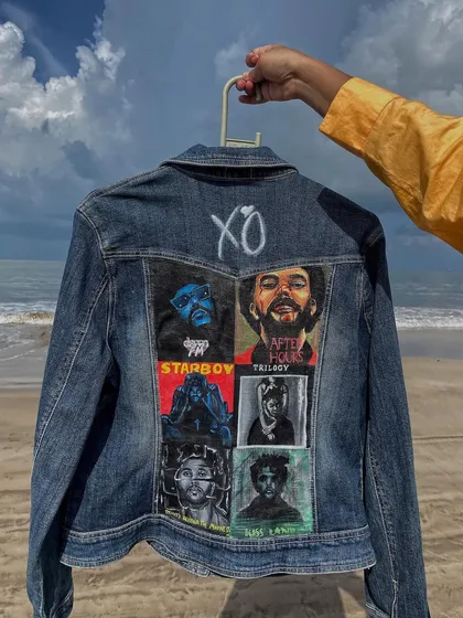 Holding up the finished Weeknd jacket, this shot showcases the entire piece, from the hand-painted 'XO' at the top to the detailed portraits below.
