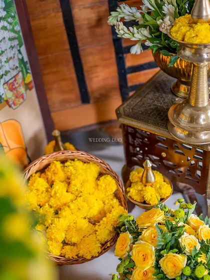 A close-up of the Haldi ceremony details. Baskets of fresh marigolds and yellow roses are ready for the rituals, set beside ornate brass vessels.