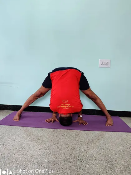 Prasarita Padottanasana with the head on the floor and hands between the feet, showing a deeper stage of the forward bend.