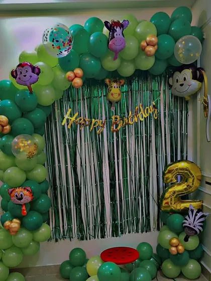 A simple jungle-themed birthday setup for a second birthday, using a green foil curtain, an animal-themed balloon arch, and a number '2' foil balloon.