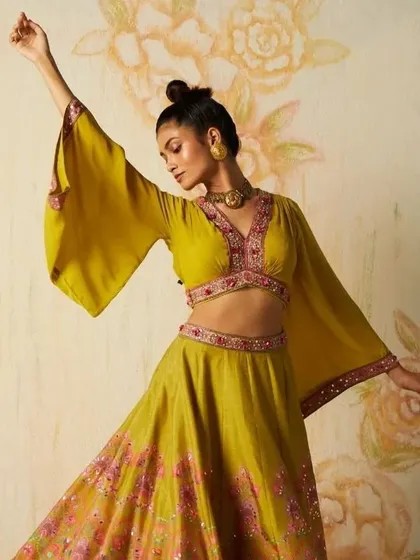 A dynamic shot from a fashion lookbook that captures movement and energy. The makeup features glowing skin and a defined top-knot hairstyle, ensuring the model looks striking while allowing the designer's vibrant, flowing garment to be the star.