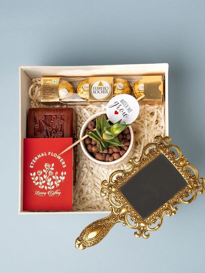 A top-down view of the contents of the naming ceremony return gift, including a succulent, a wooden box, Ferrero Rocher, and a hand mirror.