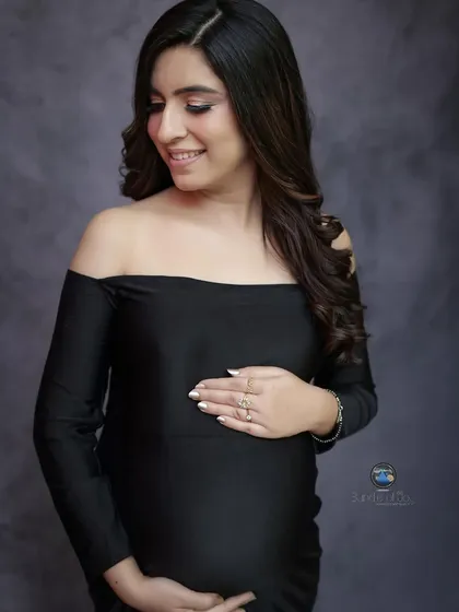 A fitted black gown can create a stunningly elegant and modern maternity portrait. This off the shoulder, mermaid style dress beautifully accentuates her form, while her gentle smile adds a touch of warmth.