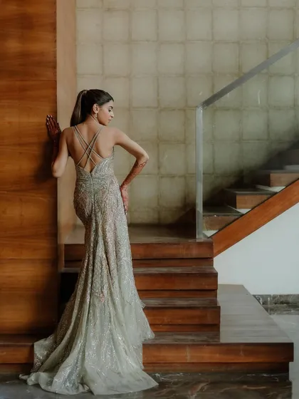 A stylish and modern bridal portrait. The backless design of her shimmering gown and the clean lines of the wooden staircase create a sophisticated and contemporary image.