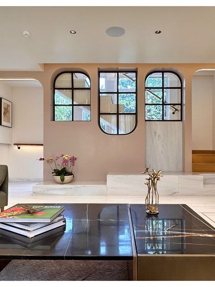 From the main living area, the arched windows on the mezzanine level act as internal balconies, enhancing the sense of openness and connection between floors. The soft pink wall color adds a gentle warmth to the space.