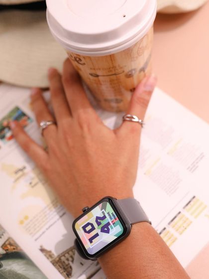 Wearables meet aesthetics. This lifestyle shot shows the boAt Xtend Plus smartwatch on the wrist in a cozy, everyday setting with coffee and a magazine, highlighting its stylish design.