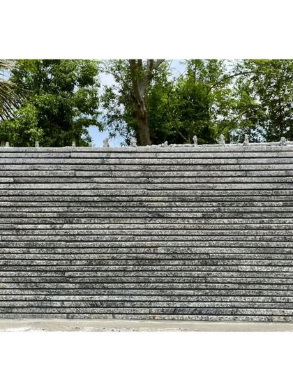 The finished texture of the Nandi House wall, built from waste granite off-cuts. The horizontal lines create a strong graphic quality against the lush green landscape.