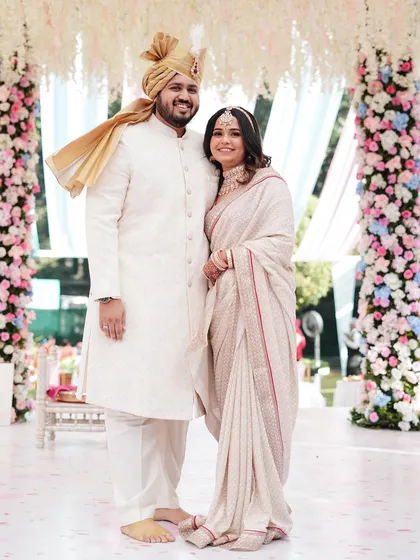 A full-length portrait showcasing the couple's elegant white and red outfits against a backdrop of stunning floral pillars. The composition is grand and celebratory.