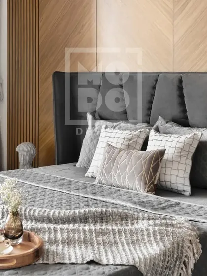This bedroom invites you to unwind with its inviting design and soothing grey tones. The layered textures of the bedding and the warm wood accent wall create a personal haven for relaxation.
