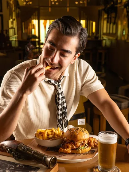 A man enjoying a burger and fries at a pub. This candid moment feels authentic and captures the simple pleasure of good food.