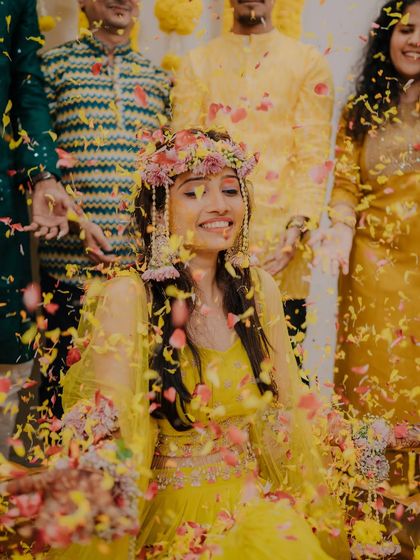 A radiant bride enjoying a shower of colorful petals during her Haldi ceremony, her smile lighting up the entire frame.