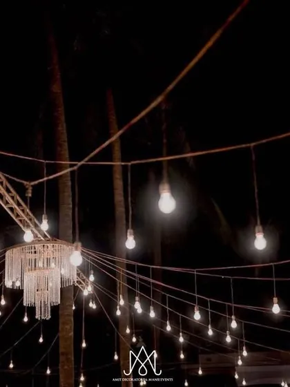 The custom chandelier and string light installation seen from below, set against the dark night sky and palm trees.