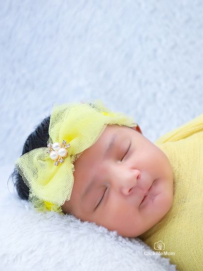 A close-up of a sleeping baby's face, framed by a delicate yellow bow. You can see the soft curve of her lips and the smoothness of her skin.
