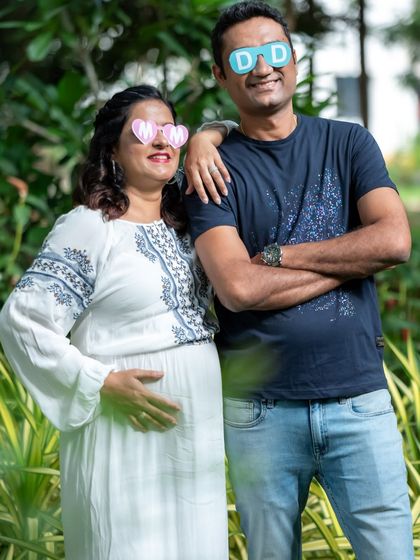 A fun and casual couple's portrait with "MOM" and "DAD" glasses in a park.