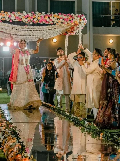 A beautiful bridal entry under a 'phoolon ki chadar' held by her brothers, walking down a mirrored aisle. A perfect blend of tradition and modern elegance.