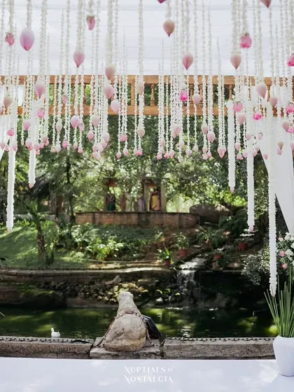 A mandap with a ceiling of hanging lotus buds and white curtains, creating a truly magical and dreamlike setting over the pond.