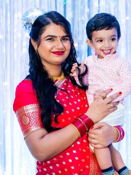 A mother holds her son, both dressed in festive traditional wear, posing for a photo at his first birthday party.